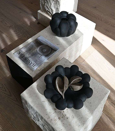 Artystyczne czarne misy ceramiczne na minimalistycznych kamiennych stołach o naturalnej fakturze.