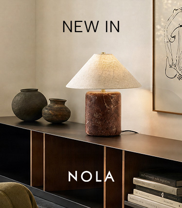 Lampa stołowa Nola z czerwonobrązową marmurową podstawą i stożkowym lnianym kloszem na ciemnej komodzie. Tekst: „Nowość – Nola”.