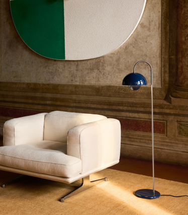 Elegancka lampa podłogowa &Tradition obok nowoczesnego fotela lounge w przytulnym wnętrzu.
