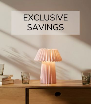 Bladoróżowa lampa stołowa na drewnianym kredensie, otoczona szklankami i książkami w ciepłym świetle słonecznym.