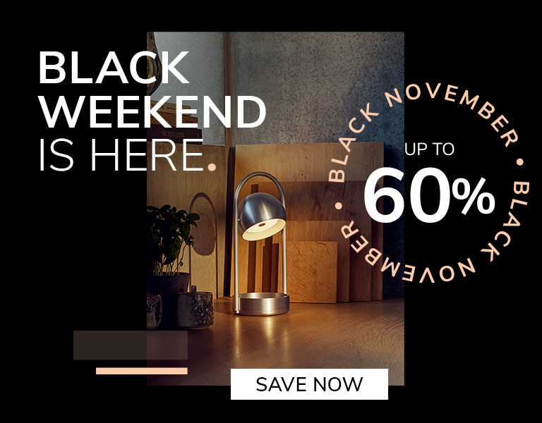 Save now Modern silver table lamp glowing on a wooden desk with cutting boards and plants in the background. Promotional text reads: ‘Black Weekend is here. Up to 60%. Black November.’ A button says ‘Save Now.